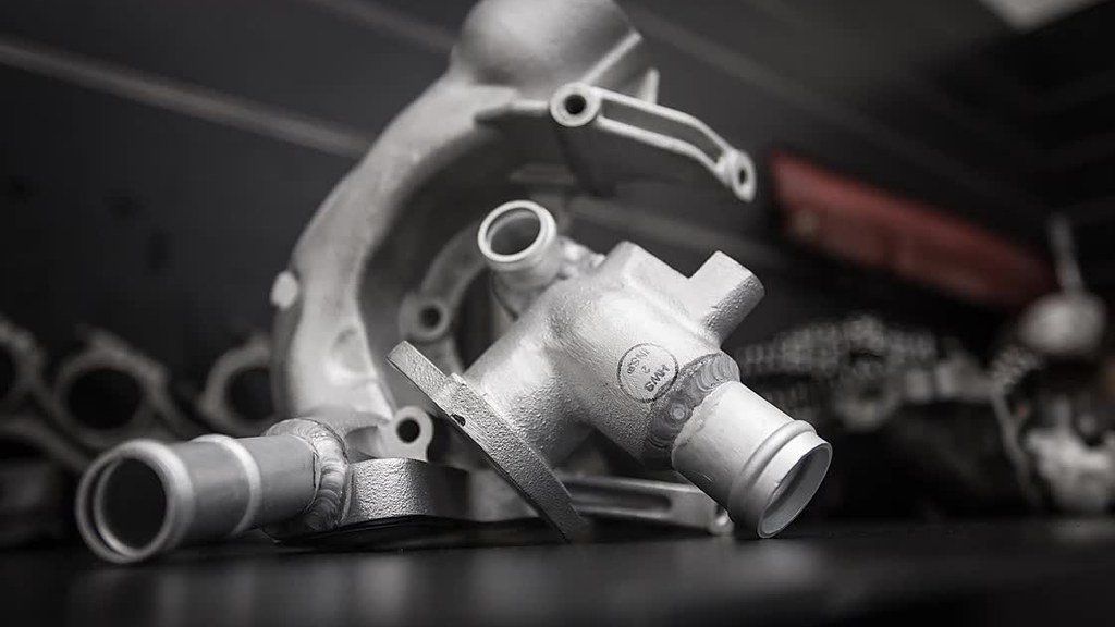 Silver metal pipe fittings and valves arranged on a dark surface, with blurred industrial equipment in the background