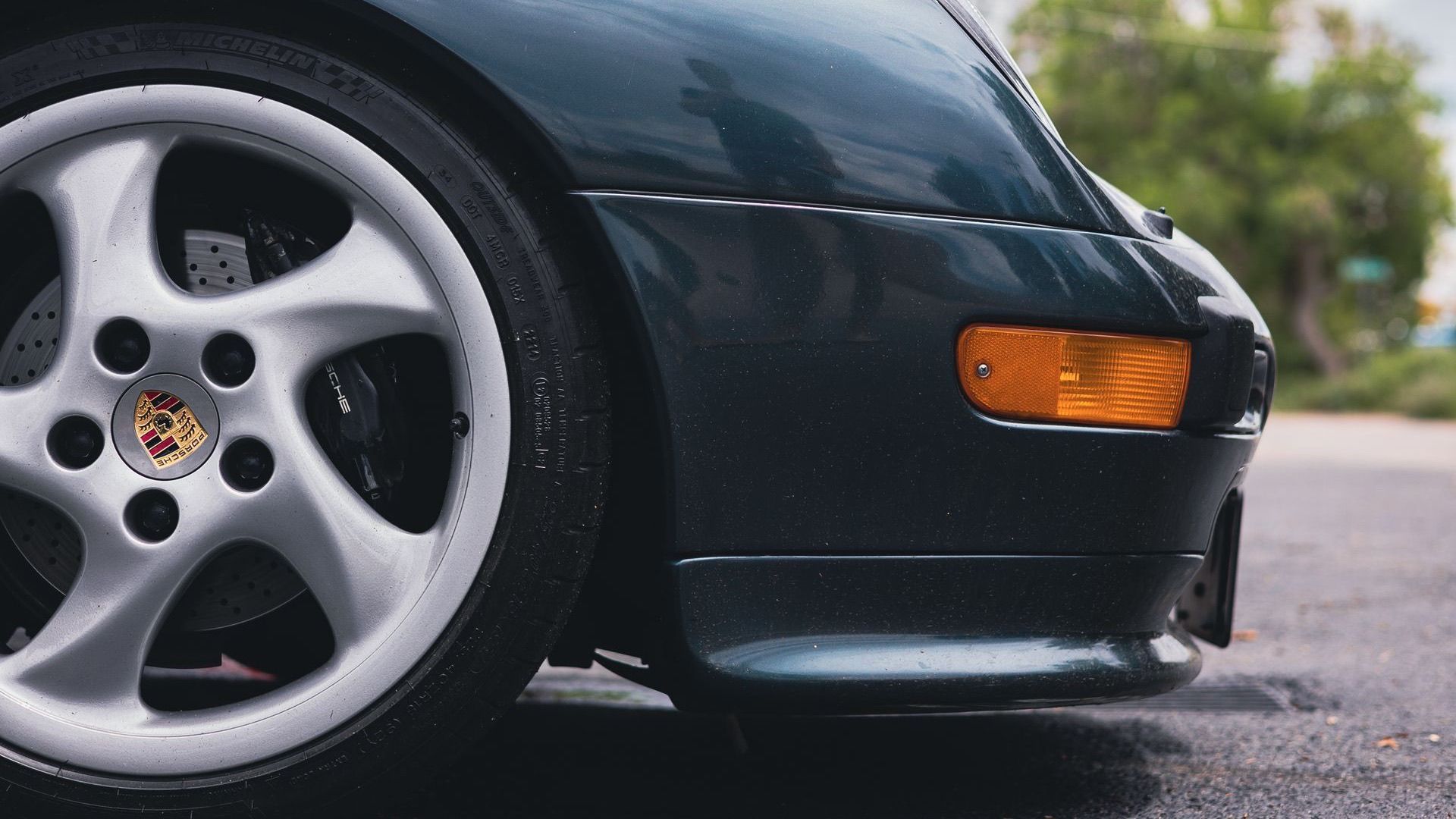 Dark green Porsche front wheel with a cross-drilled brake rotor and a black Porsche caliper visible through the spokes
