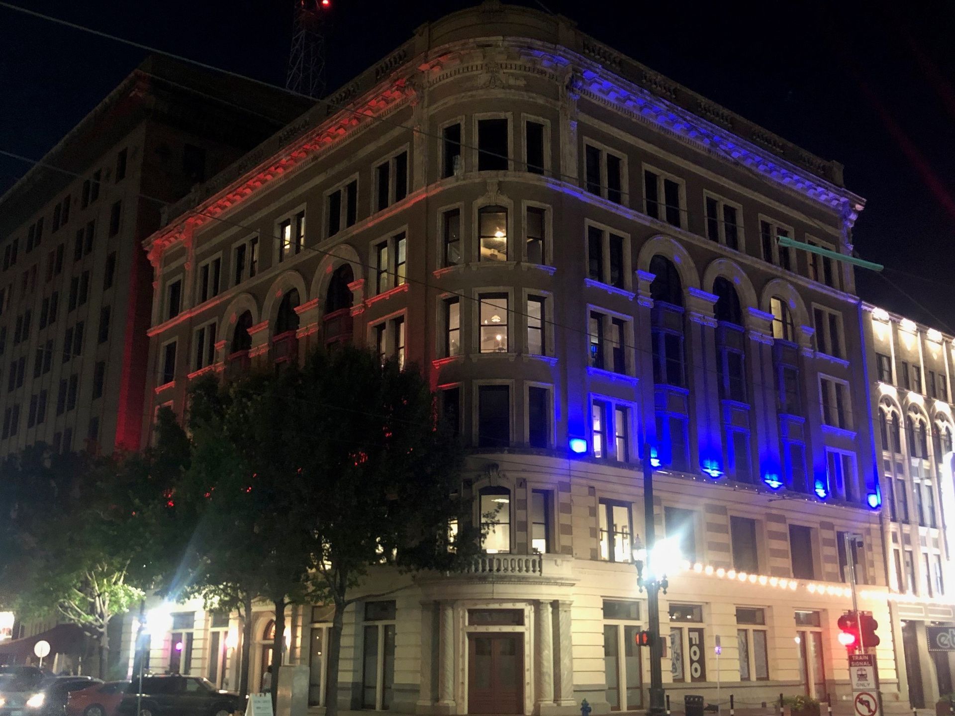 A large building is lit up with red , white and blue lights at night.