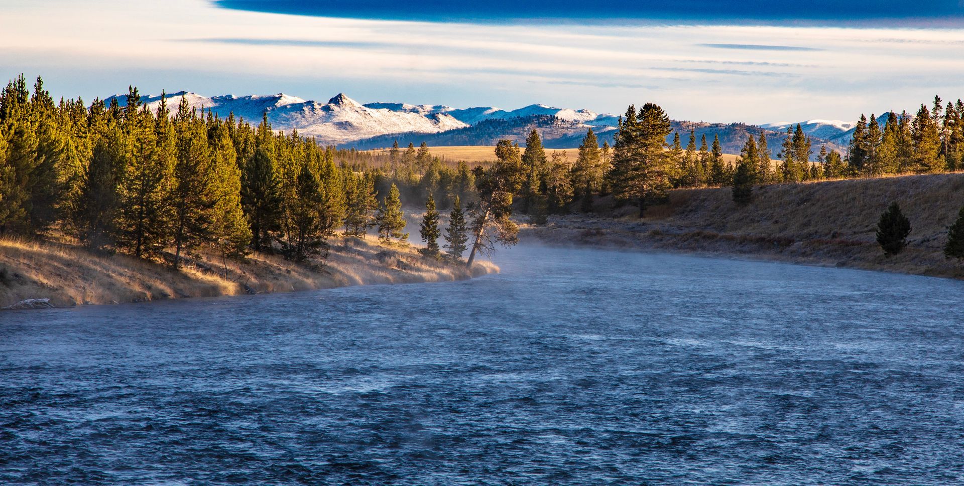 Snow-covered mountain valley with pine trees and a frozen lake under a clear sky