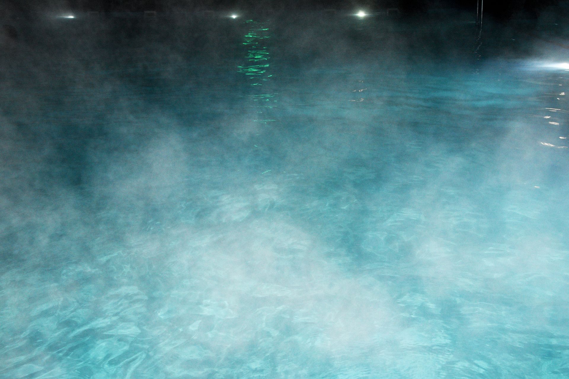 Steamy blue pool water with green underwater lights at night