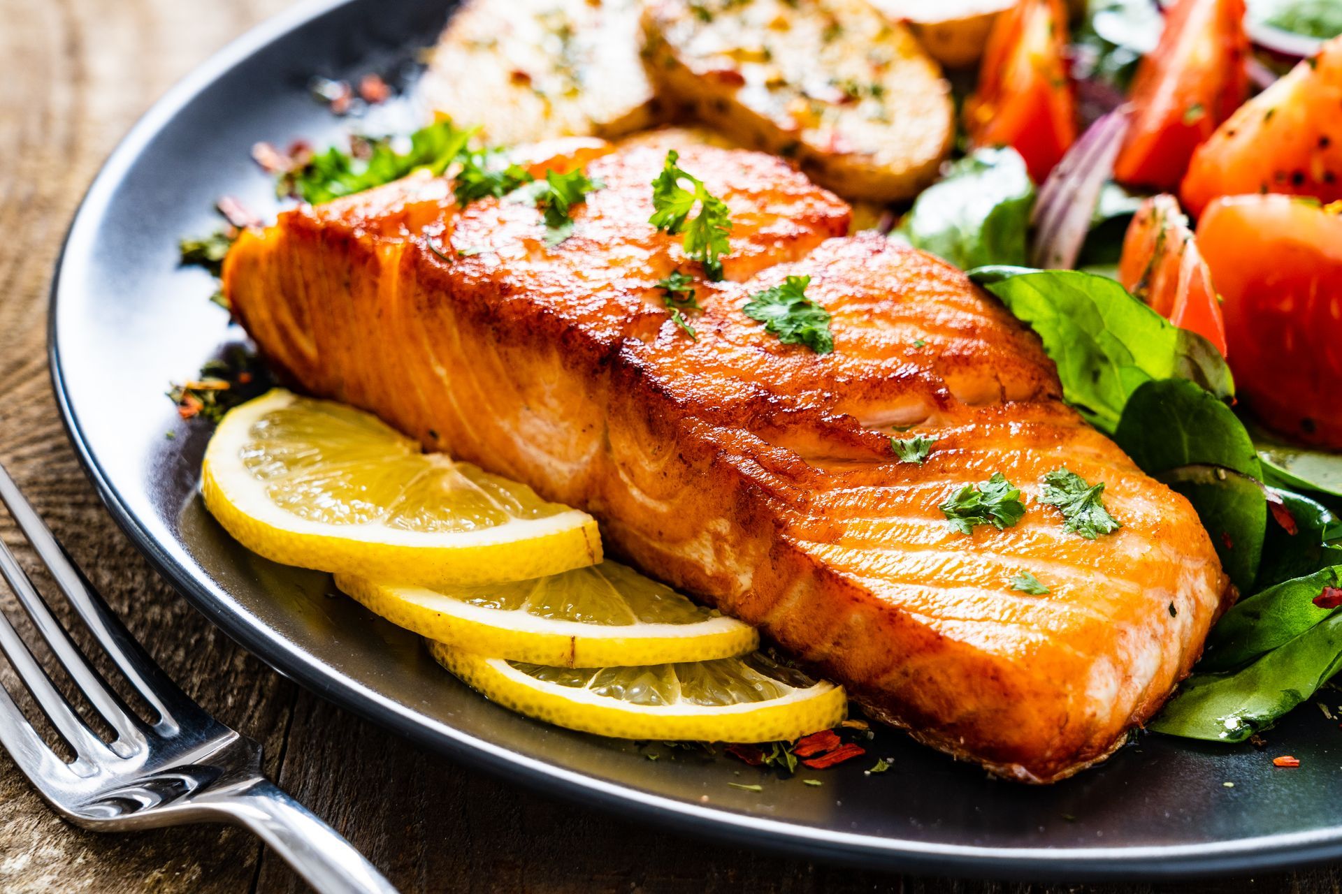 Grilled salmon fillet with lemon slices and vegetables on a dark plate