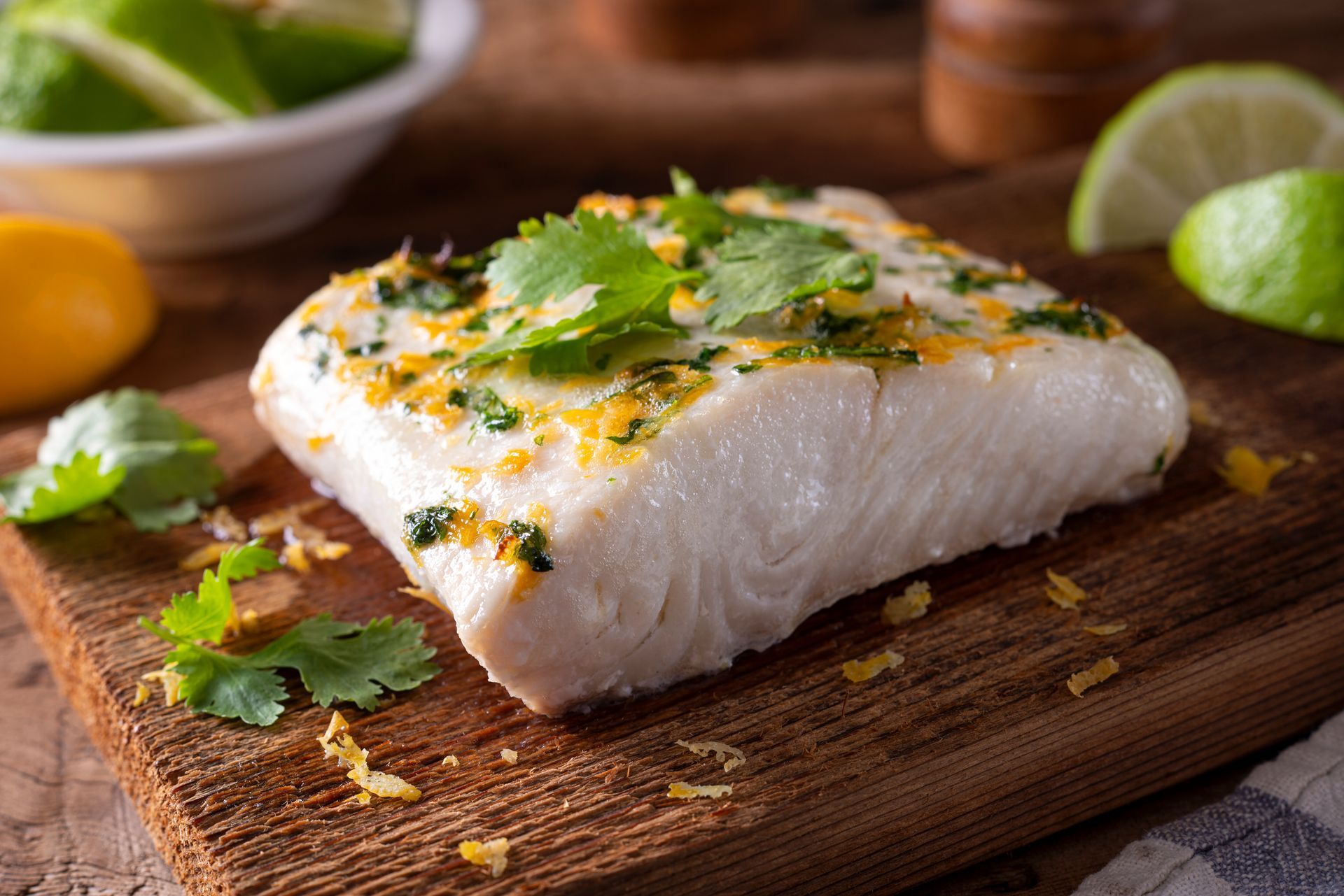 Seasoned white fish fillet on a wooden board with herbs and lemon wedges