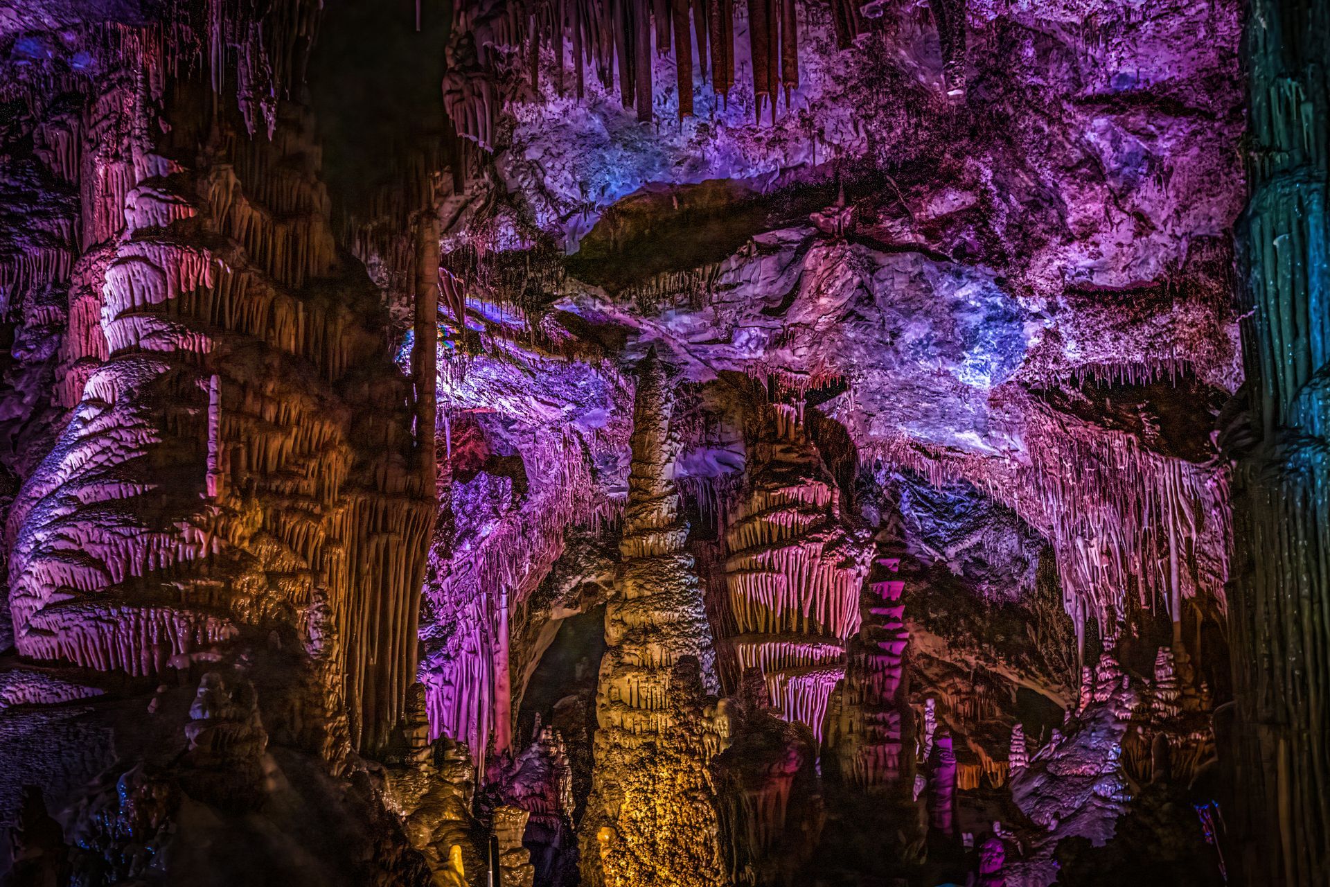 Colorfully lit cave interior with purple, pink, and amber stalactites and rock formations