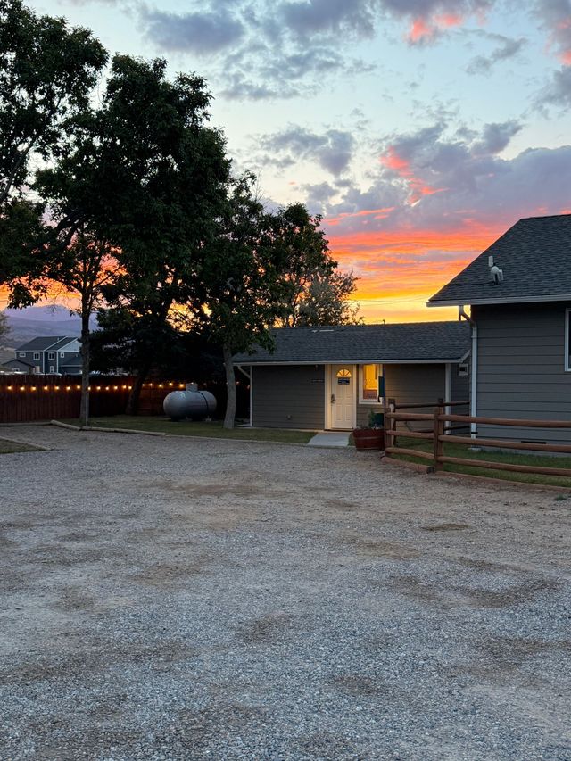 Sunset over a gravel courtyard with trees, a barn, and a fenced farmhouse