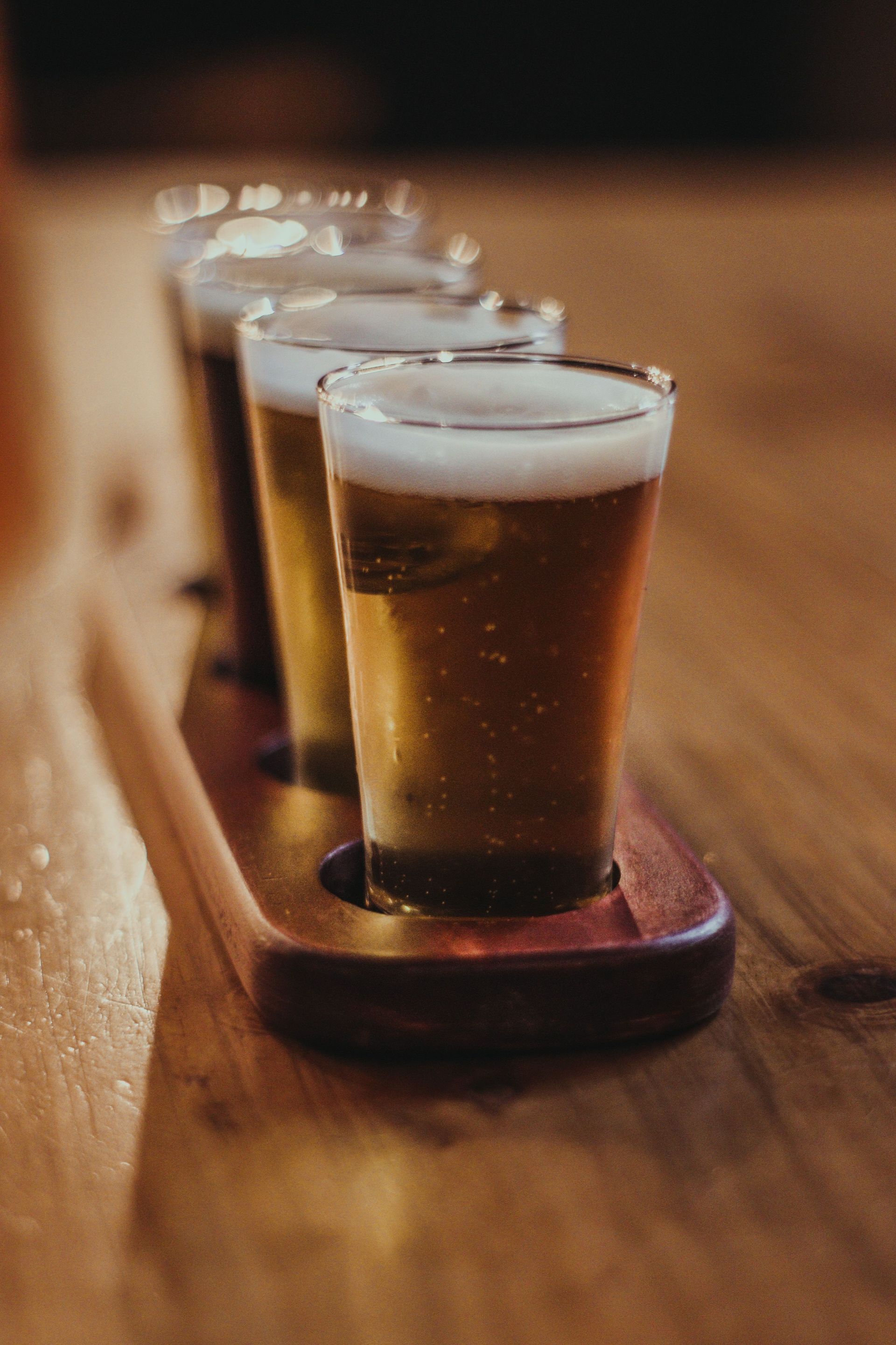Three small beer samples in clear glasses on a wooden serving tray