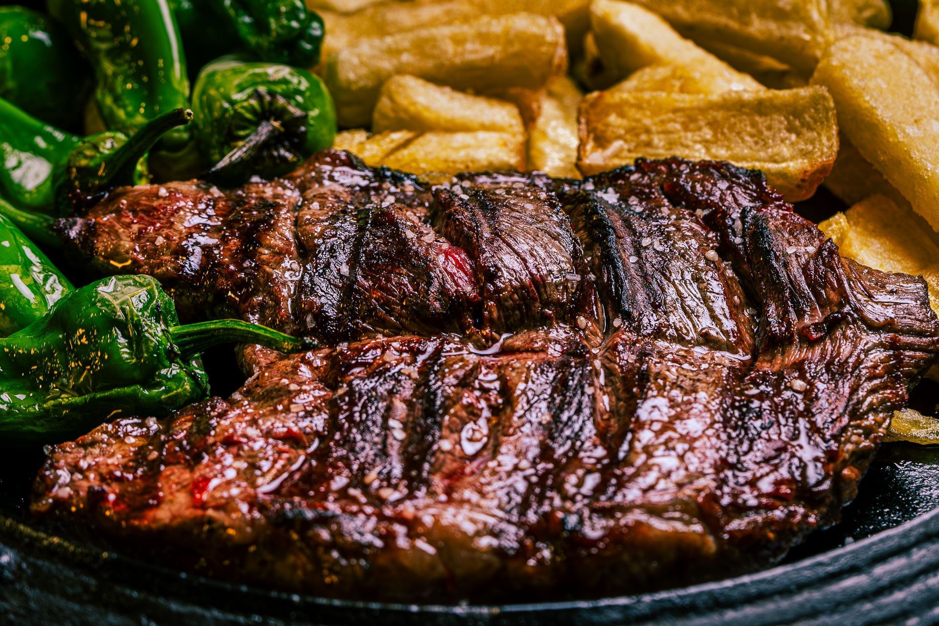 Grilled steak with greens and fries on a black plate