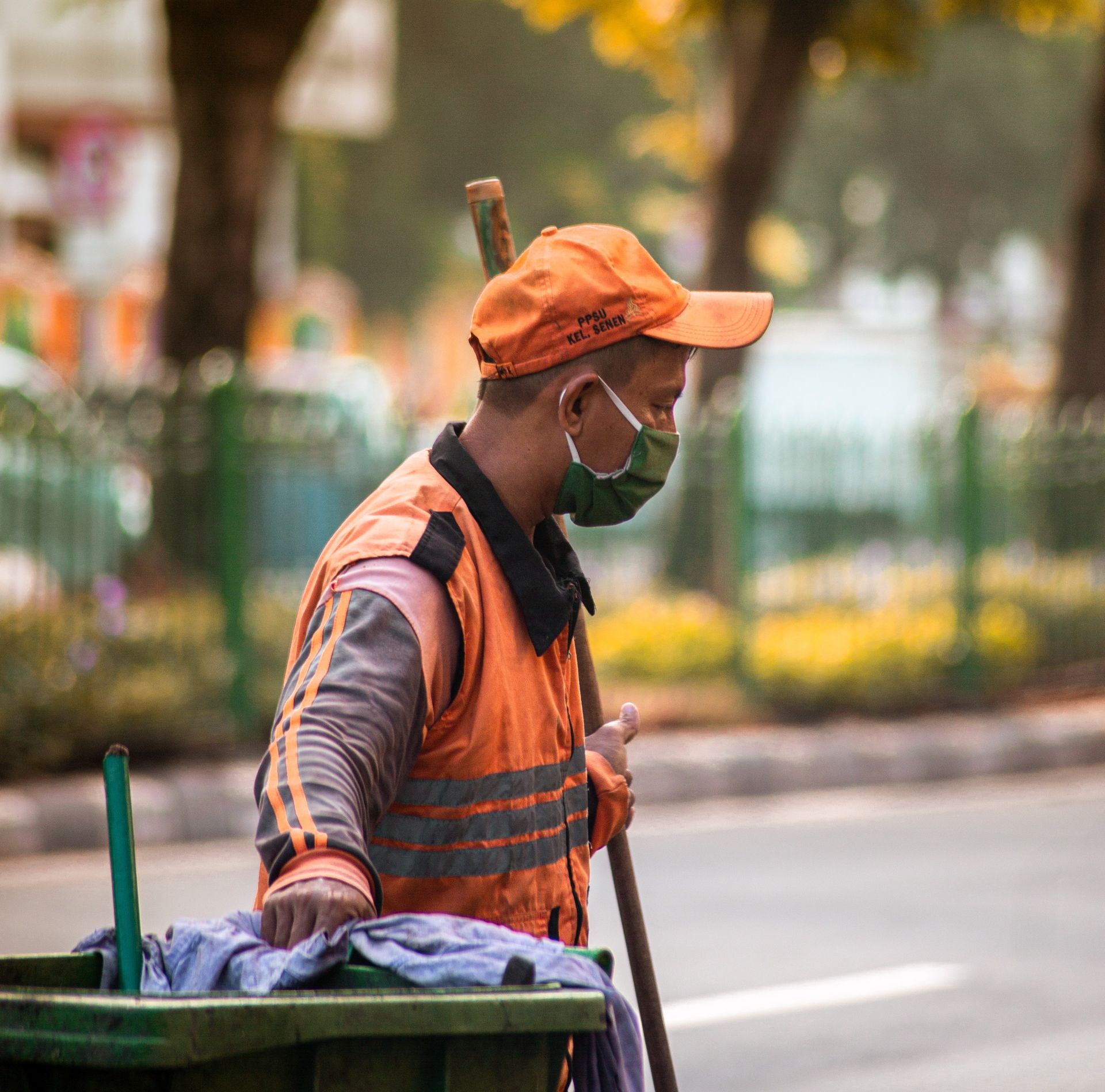 a man wearing a mask and an orange hat is cleaning a trash can .