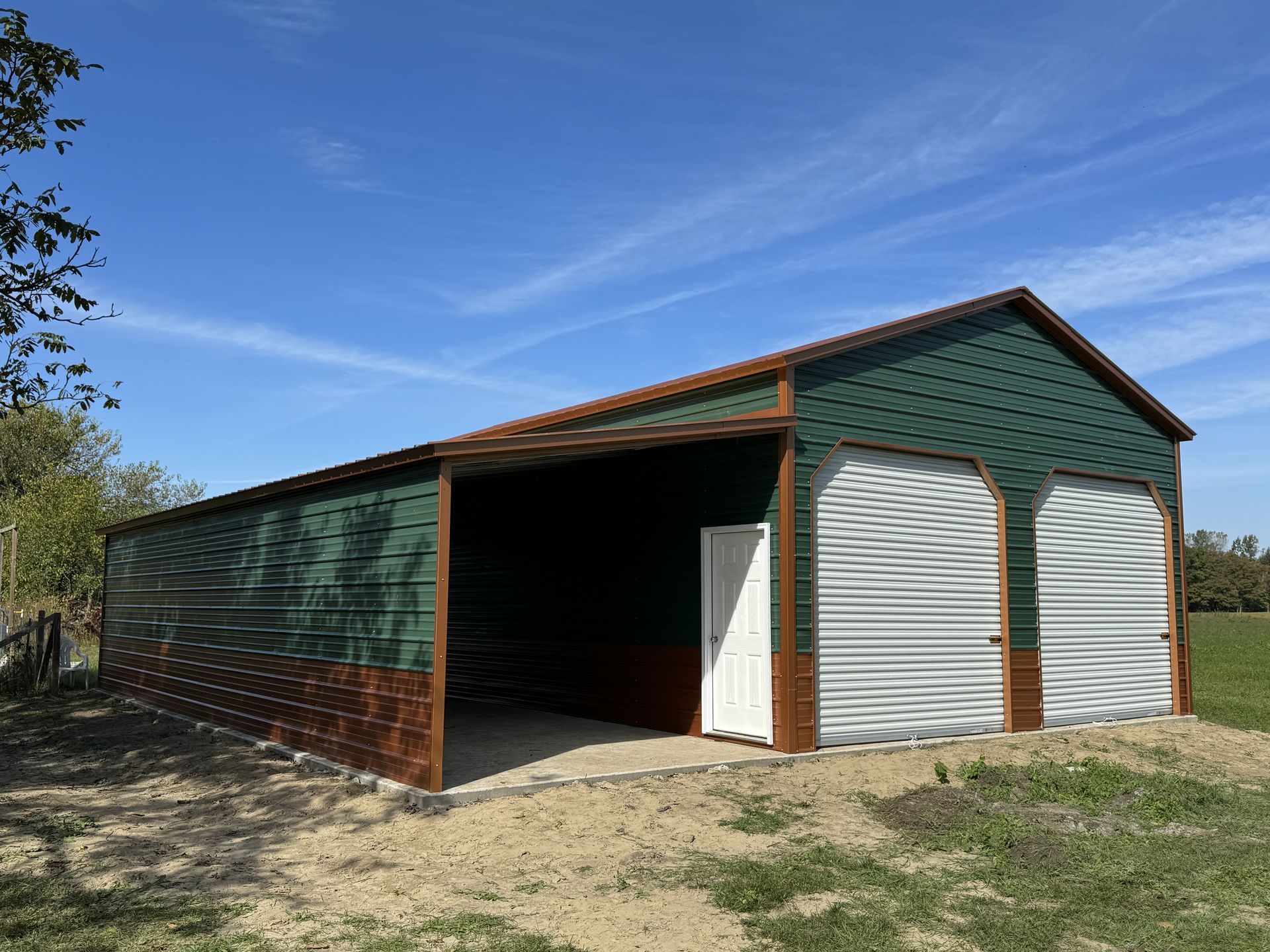 A green garage with a white door is sitting in the middle of a field.