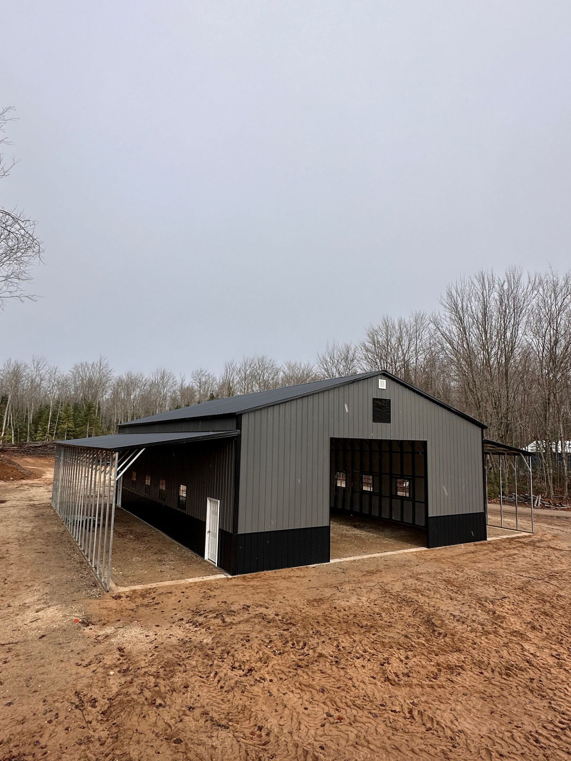A large metal barn is sitting in the middle of a dirt field.