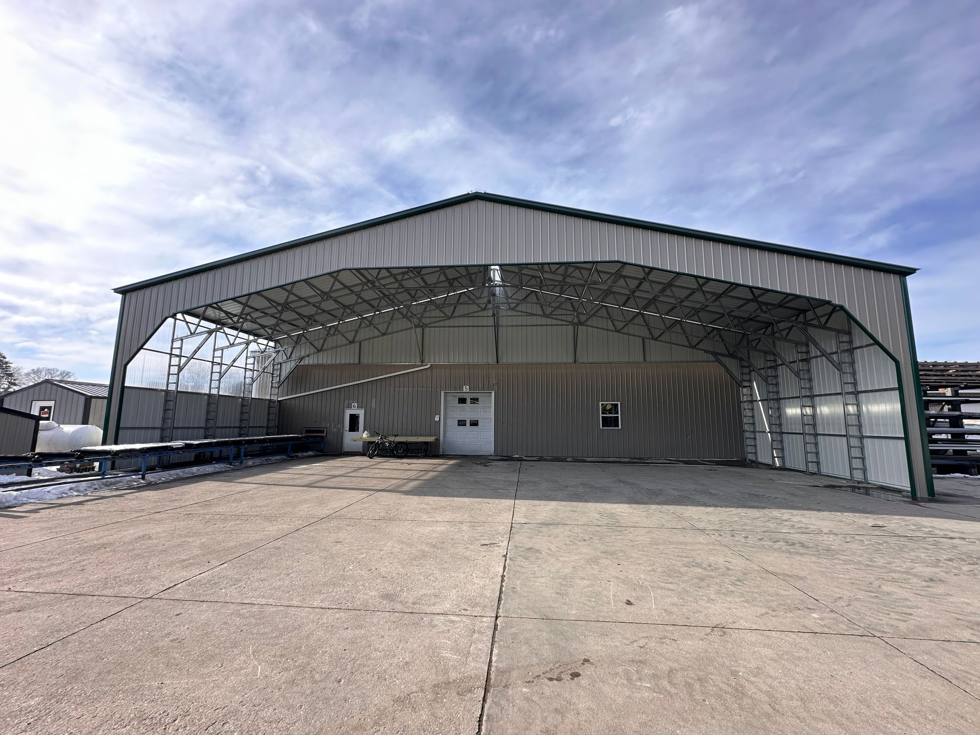 A large metal building with a roof is sitting on top of a dirt field.