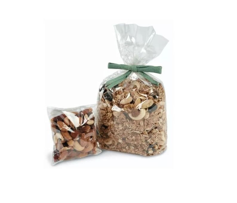 Dos bolsas transparentes con una mezcla de frutos secos y nueces, una de ellas atada con una cinta verde, sobre un fondo blanco.