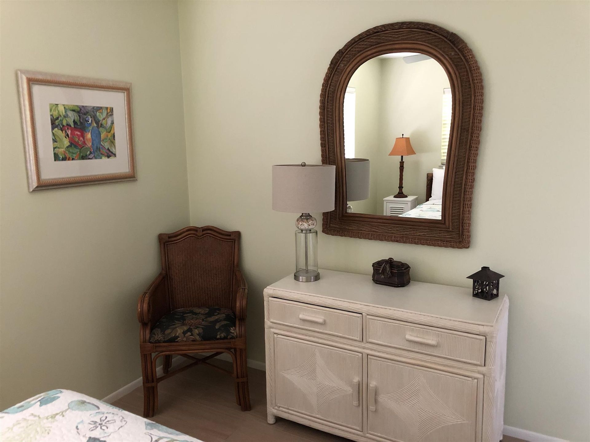 A bedroom with a dresser , chair , lamp and mirror.