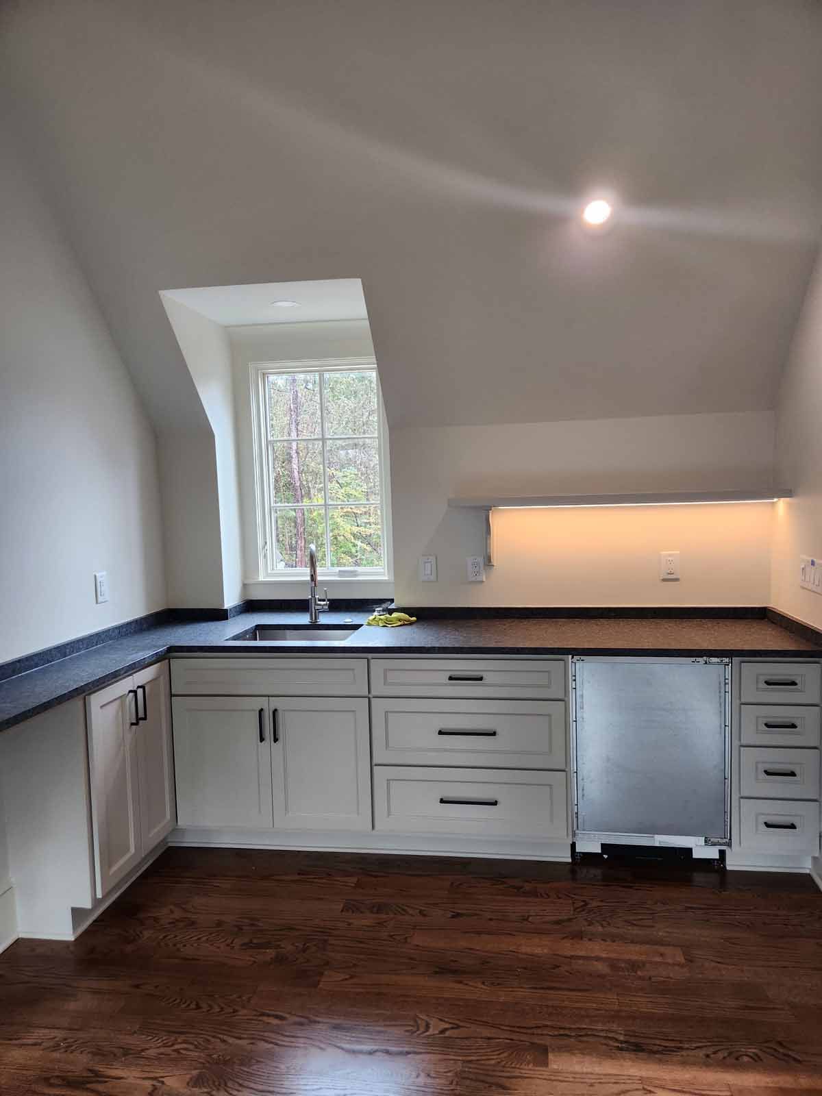 An empty kitchen with white cabinets , a sink , and a window.