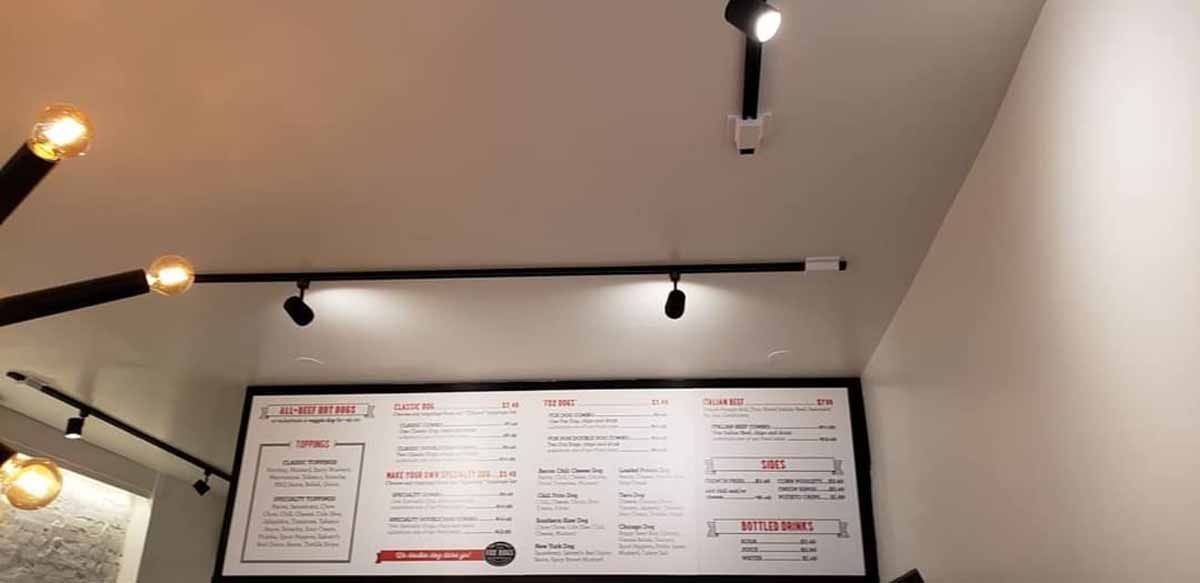 A restaurant with a menu on the wall and lights on the ceiling.