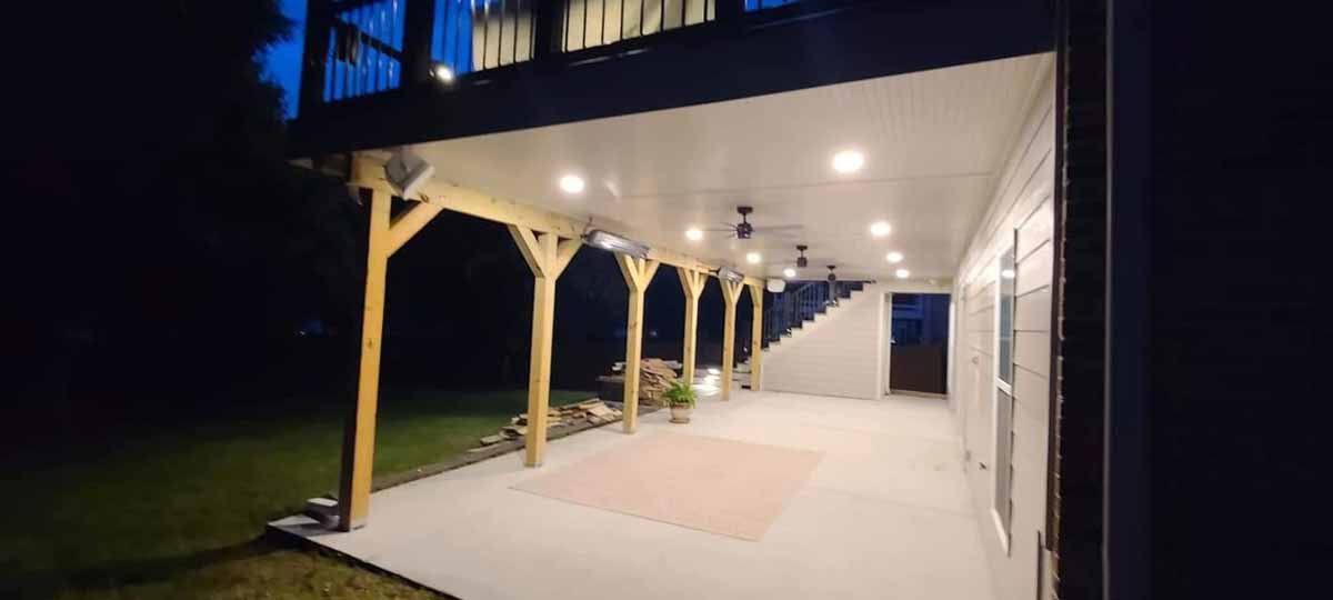 A large covered porch with a ceiling fan and lights at night.