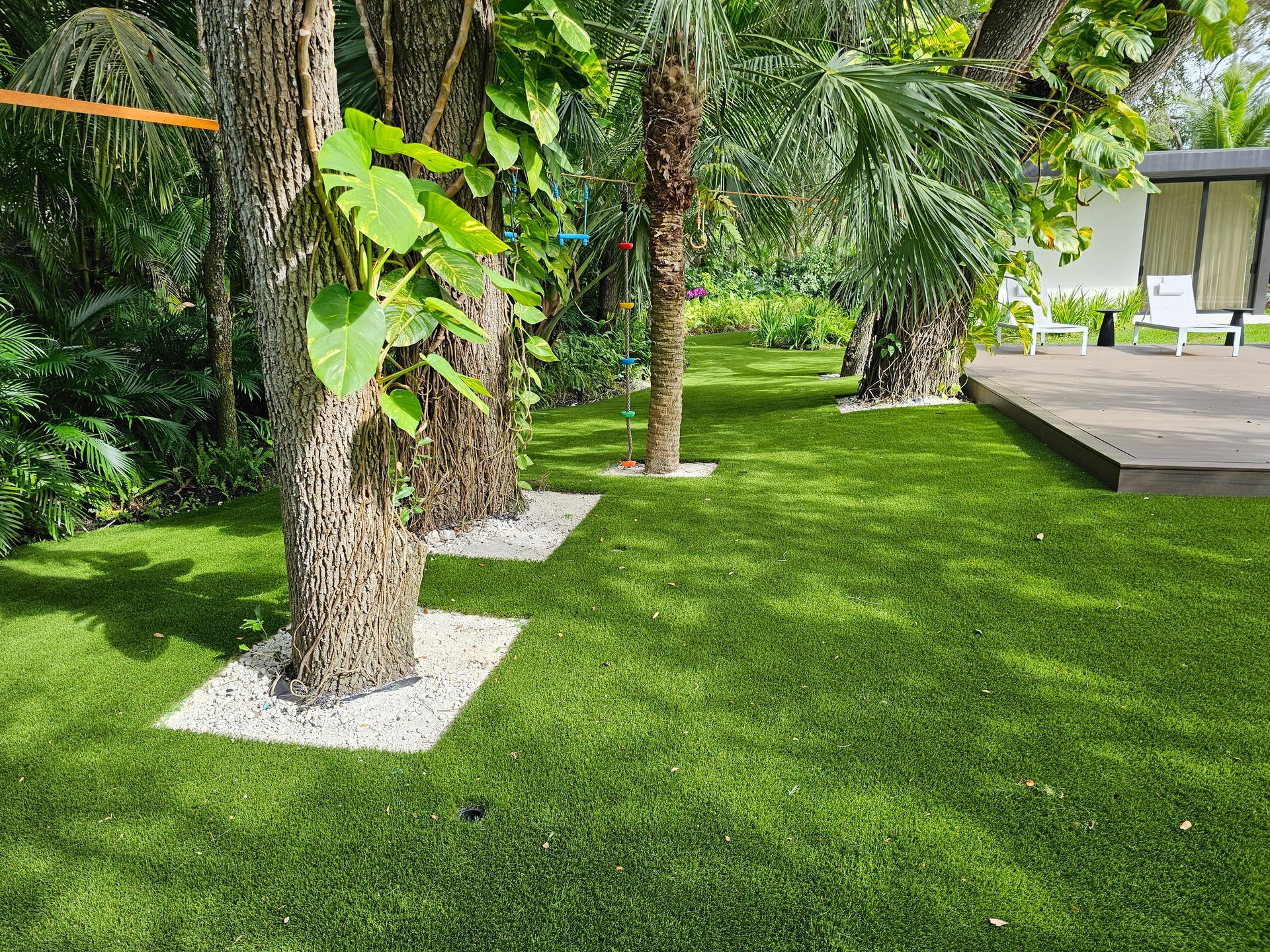Lush garden with palm trees, green lawn, and a raised deck beside a white building