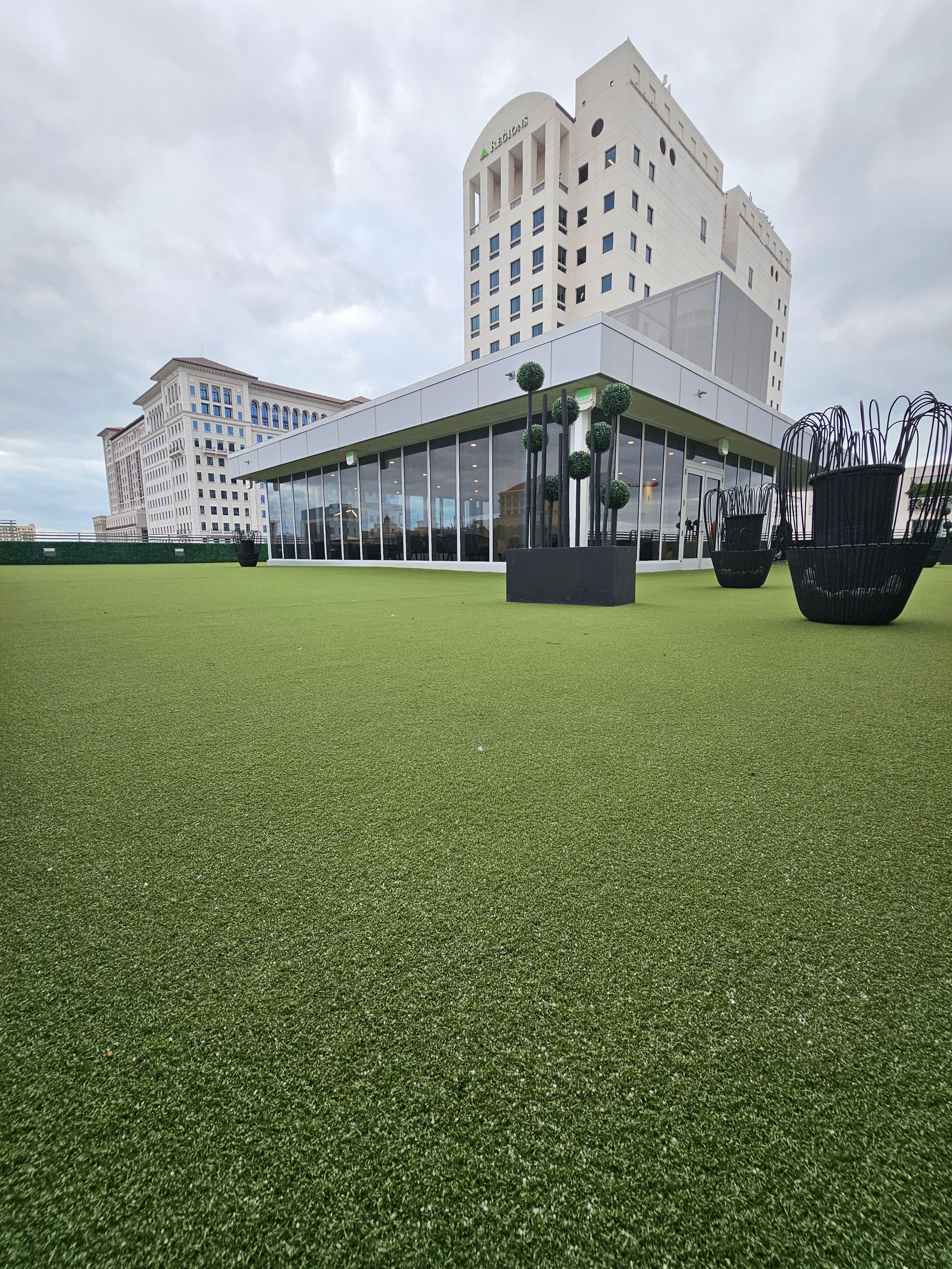 Modern white hotel buildings behind a wide green lawn under a cloudy sky