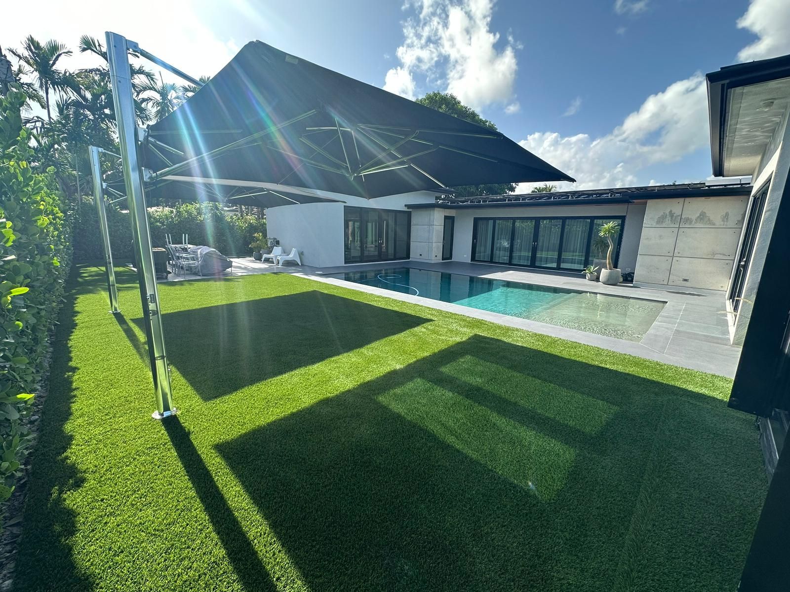 Modern house with solar panels, green lawn, and a swimming pool under a bright blue sky