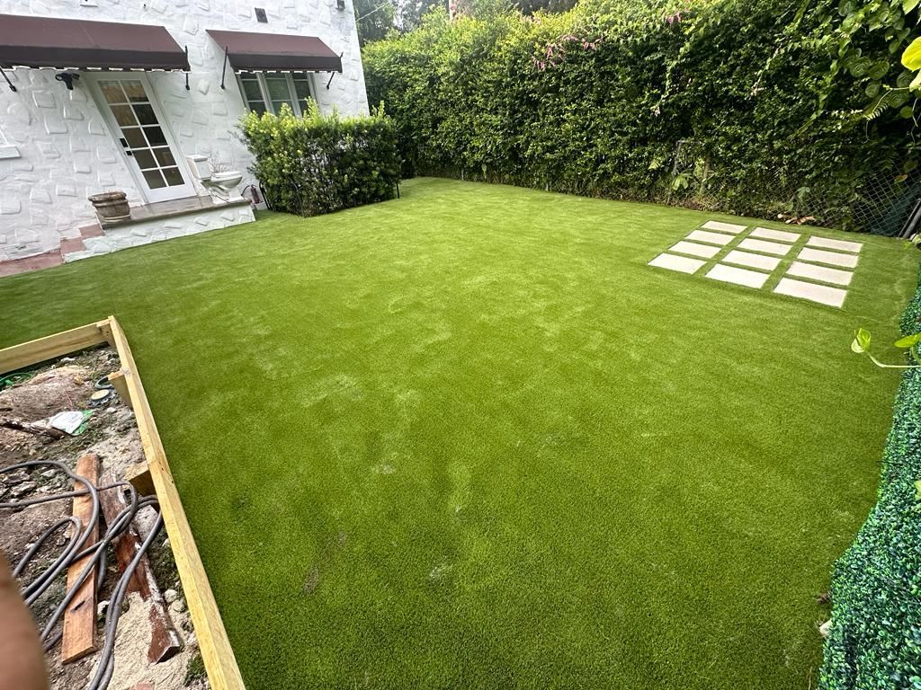 Backyard lawn with bright green grass, hedge border, and stone stepping pads beside a house