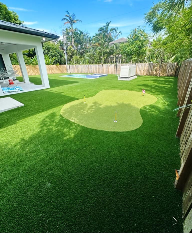 Backyard with artificial turf, a putting green, patio, and wooden fence under bright sunlight