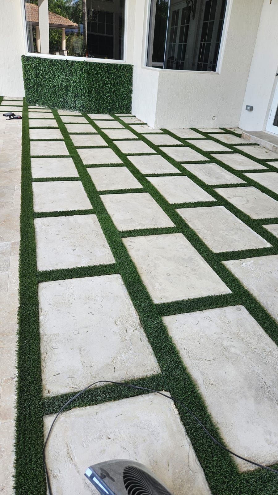 Rectangular white stepping stones set in green grass leading to a house patio doorway