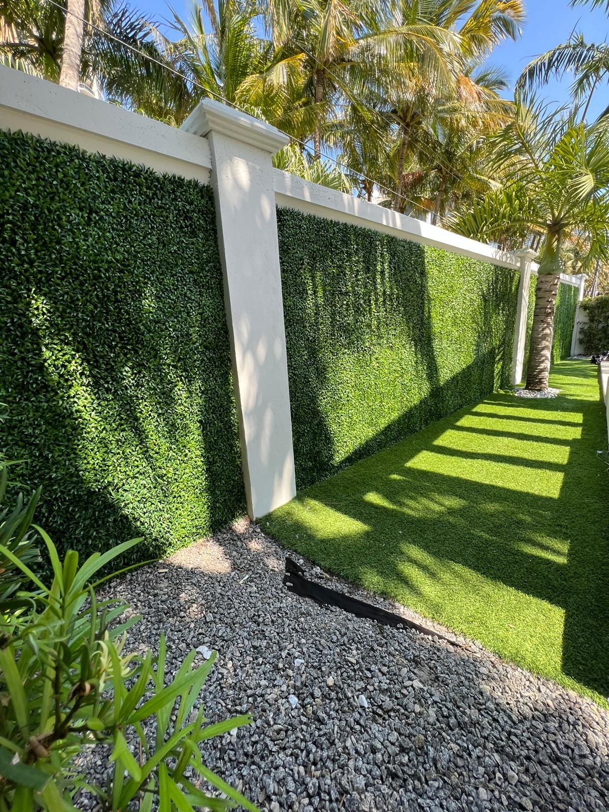 Sunlit garden wall covered with green hedges, white pillars, and trimmed lawn casting long shadows