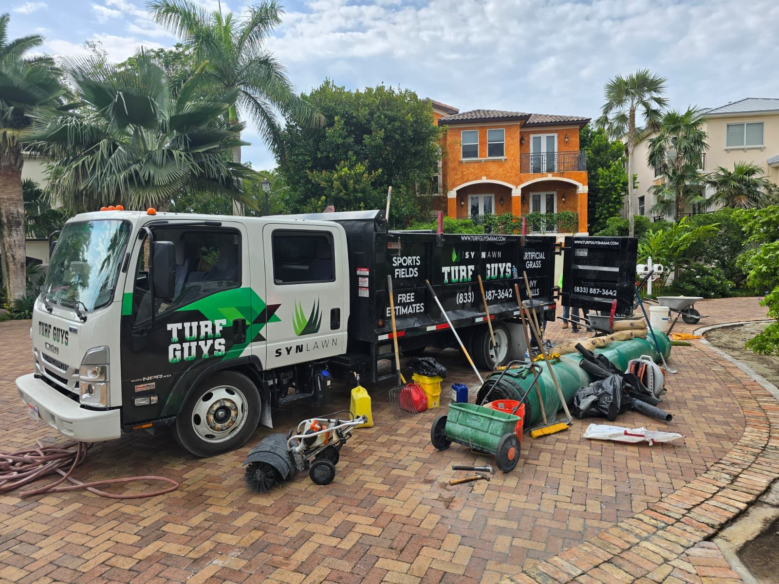 Lawn care truck with equipment on a brick driveway, in front of a two-story house.