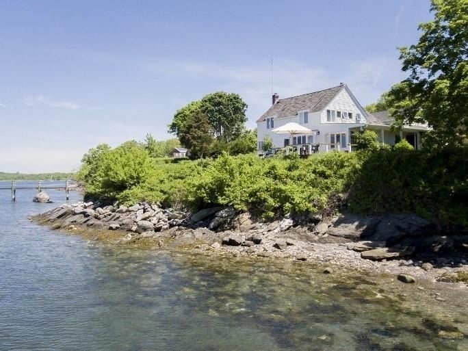 White house on rocky shoreline beside calm water under a clear blue sky