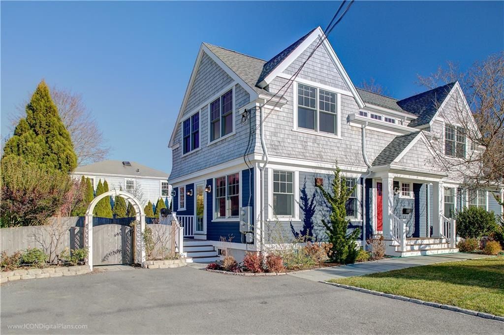 Two-story gray house with white trim, arched gate, and driveway under a clear blue sky