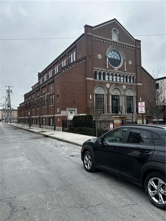 Brick industrial building on a snowy street with a black SUV parked in front.