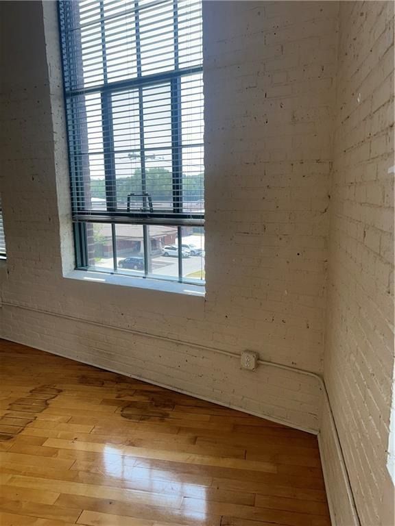 Empty room with white brick walls, large window, and hardwood floor receiving sunlight