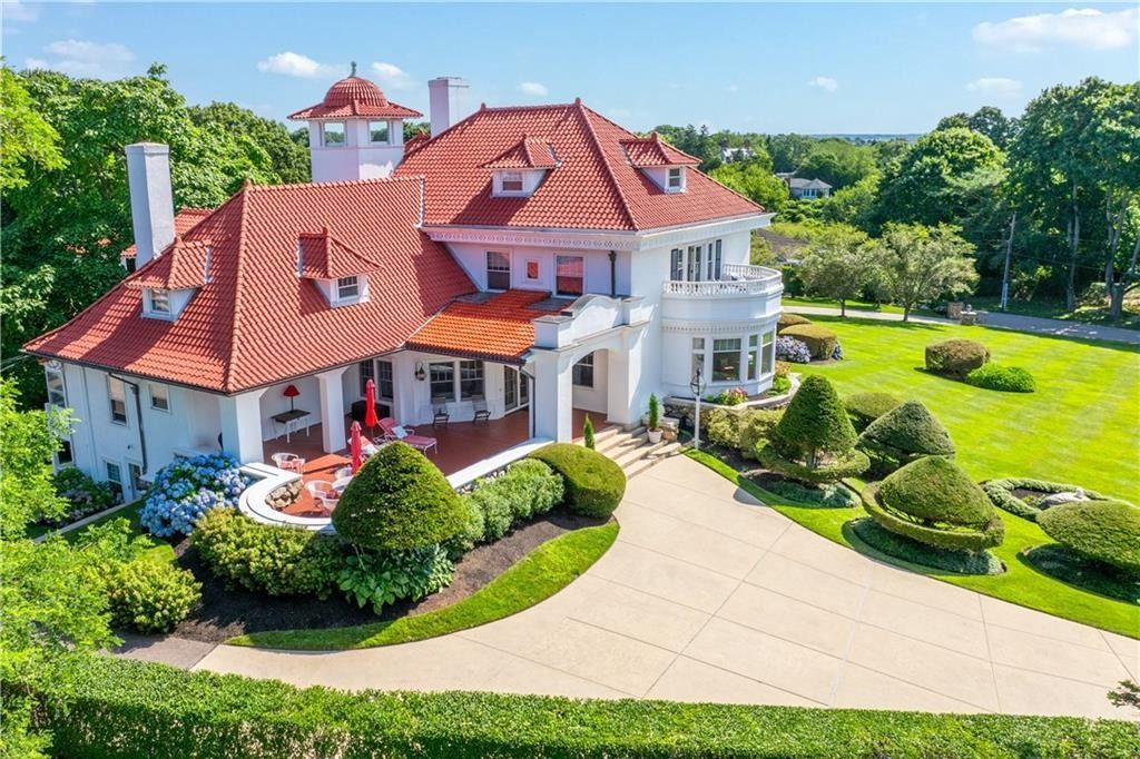 Large white house with red roof, manicured garden, and curved driveway on a sunny day