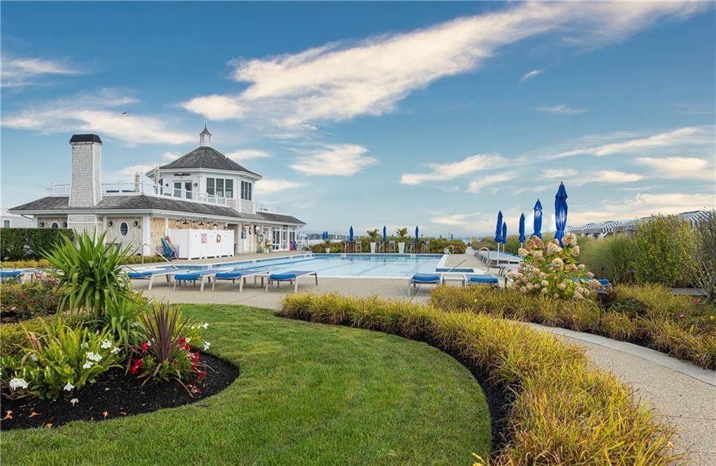 Grand white pavilion beside a garden path, reflecting pool, and blue umbrellas under a bright sky