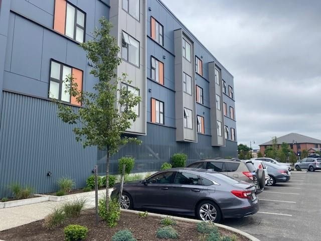 Modern apartment building with gray siding and parked cars in a lot with small trees