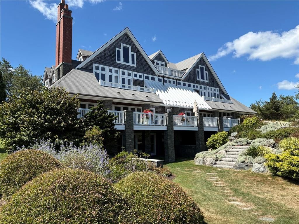 Large gray house with white trim and a red chimney, viewed from a sunny garden with stone steps and shrubs