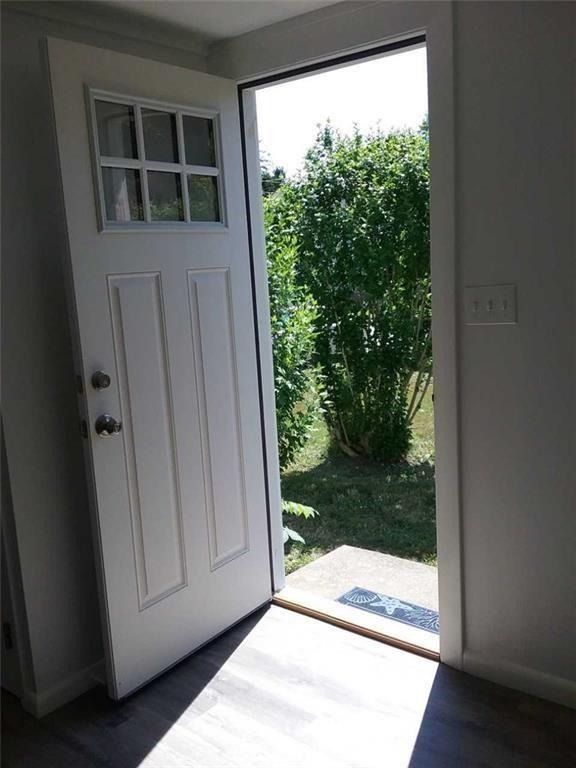 Open front door with sunlight spilling onto the floor and a view of greenery outside.