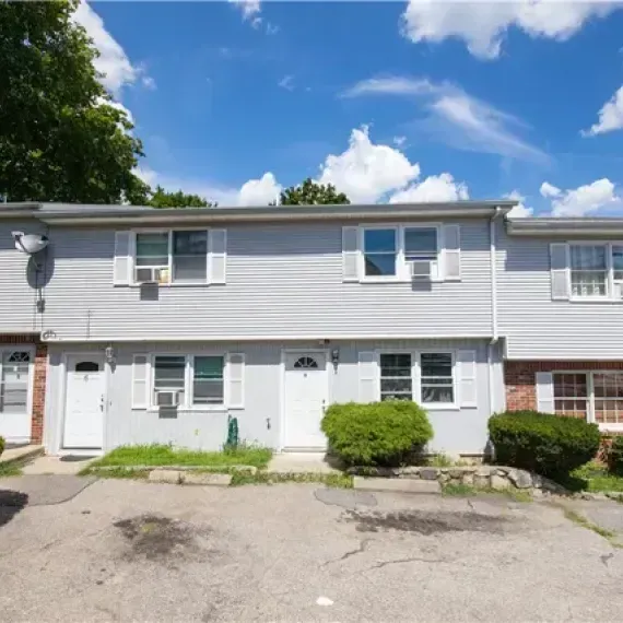 Row of gray townhouse units with white doors and windows under a blue sky