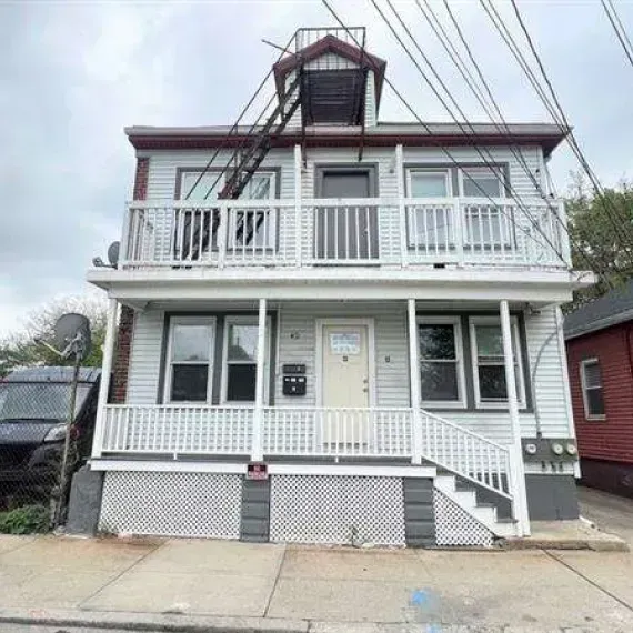 Two-story gray house with white porch railings and stairs on a city street