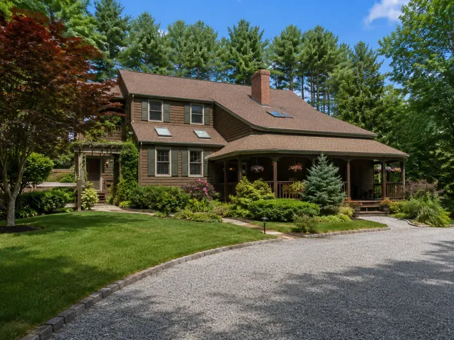 Large brown house with a covered porch, green lawn, and curved gravel driveway surrounded by trees.