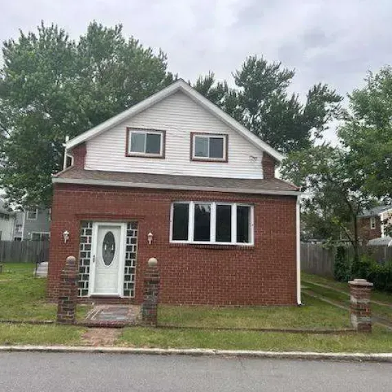 Small brick house with white upper siding, front door, windows, and a front lawn behind a curb