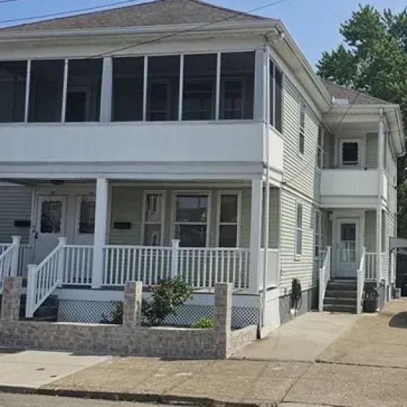 Two-story white duplex with front porches and a driveway in a residential neighborhood