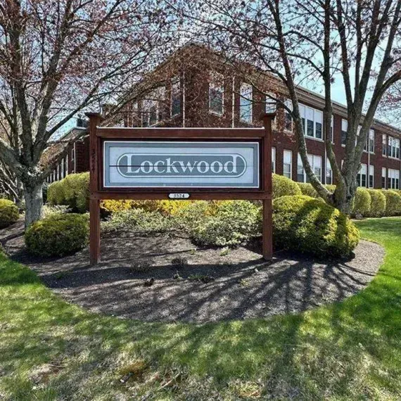 Lockwood sign in front of a brick building, with trees and shrubs in sunlight