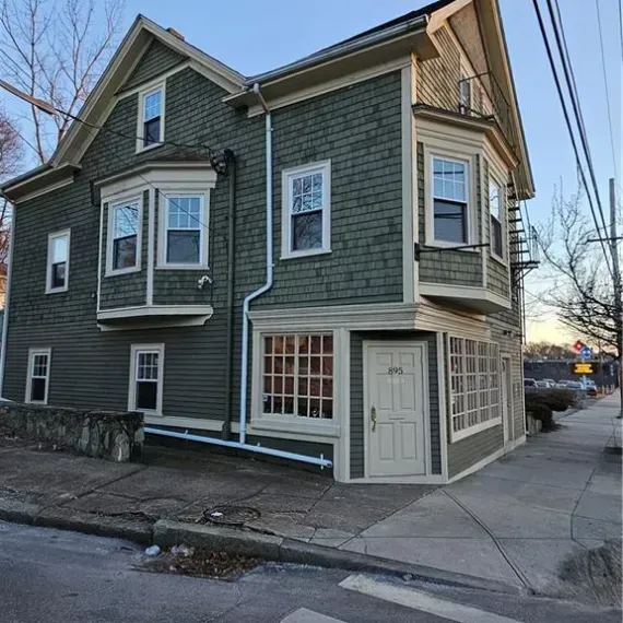 Green two-story corner house with white trim and bay windows at dusk