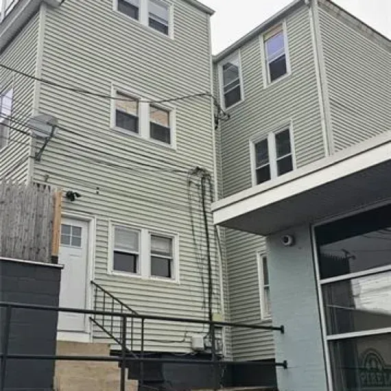 Rear view of a beige apartment building with a black metal stairway and a covered entrance