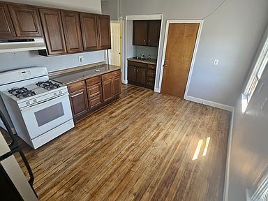 Empty kitchen with wood cabinets, white stove, and hardwood floor beside a small closet and closed door.