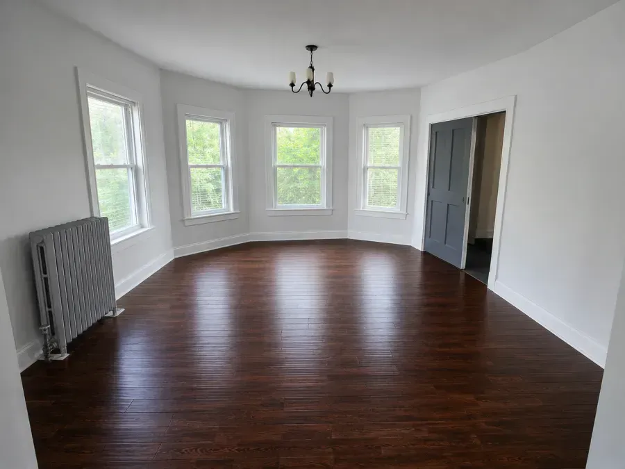 Empty bright living room with curved windows, dark wood floors, white walls, and a radiator on the left