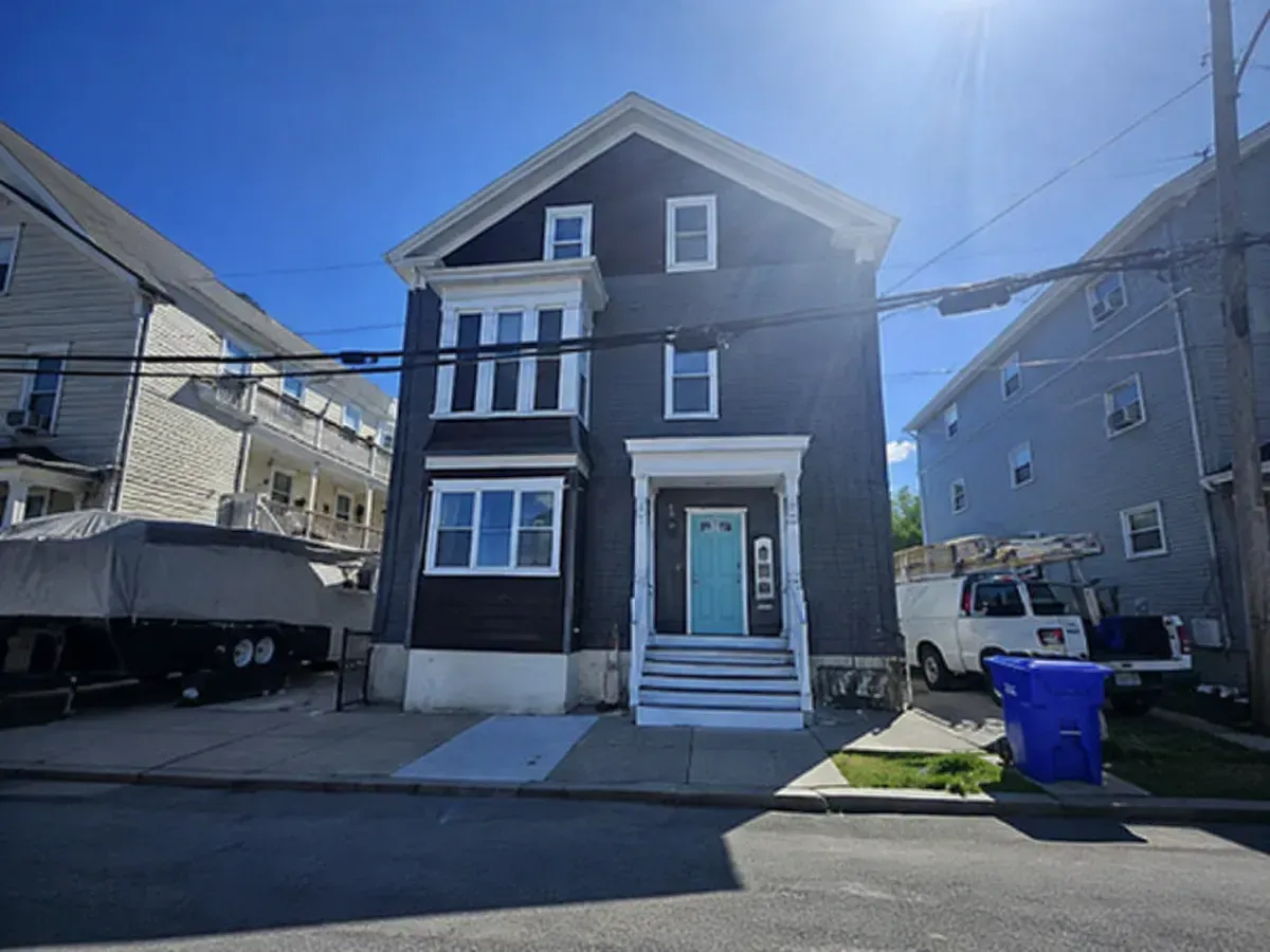 Three-story dark house with white trim and front steps on a sunny residential street