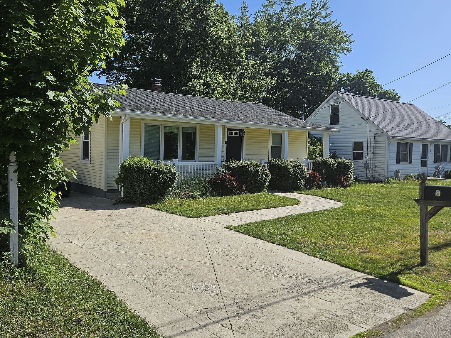 Single-story white house with a front porch, driveway, and green lawn on a sunny day