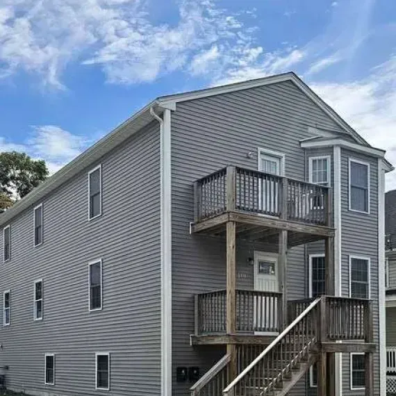 Gray two-story apartment building with balconies and exterior stairs under a blue sky